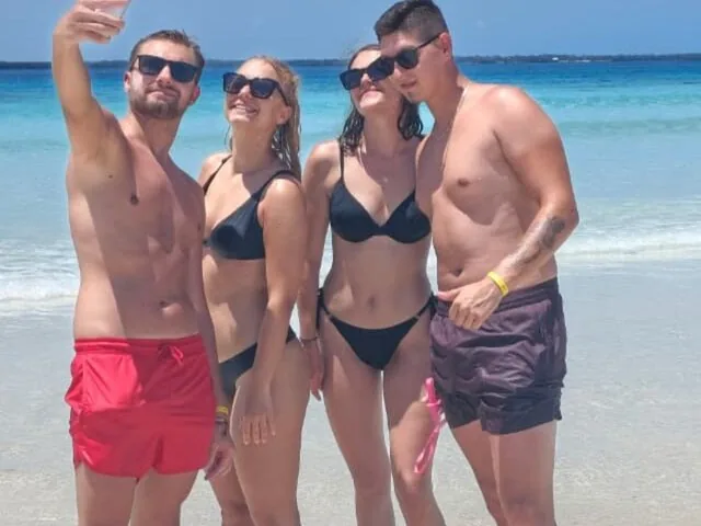 Vier Freunde, die gemeinsam auf einem sonnigen weißen Sandstrand ein Selfie machen.